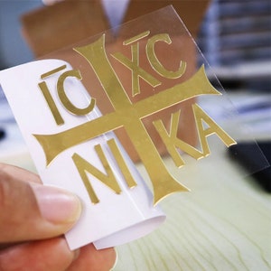 May include: Gold-coloured vinyl sticker with a cross and the words "IC XC NIKA" in a stylised font.
