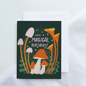 Greeting card with words "Have a magical birthday!" with trippy orange, beige, pink mushrooms (shiitake, enoki, toadstool, chanterelles) around with foliage and stars on a dark forest green background