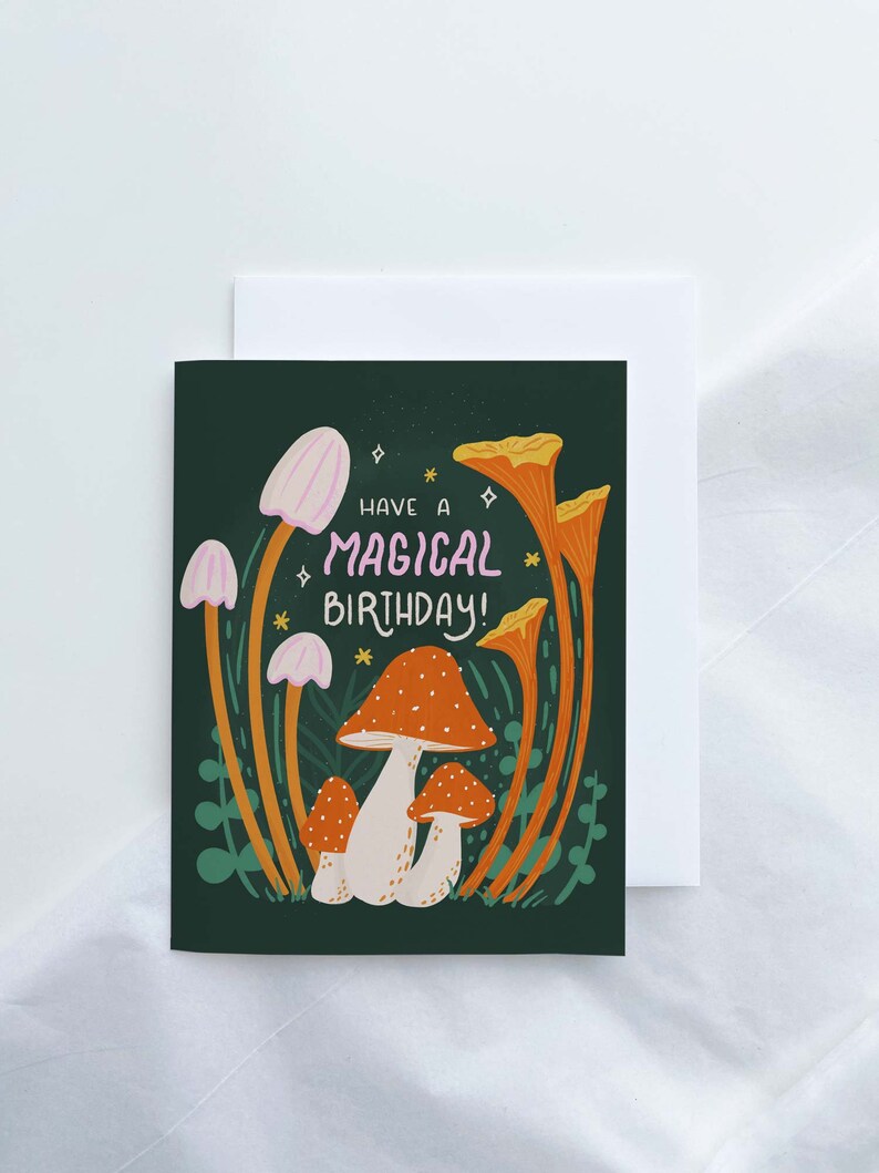 Greeting card with words "Have a magical birthday!" with trippy orange, beige, pink mushrooms (shiitake, enoki, toadstool, chanterelles) around with foliage and stars on a dark forest green background