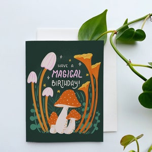 Greeting card with words "Have a magical birthday!" with trippy orange, beige, pink mushrooms (shiitake, enoki, toadstool, chanterelles) around with foliage and stars on a dark forest green background
