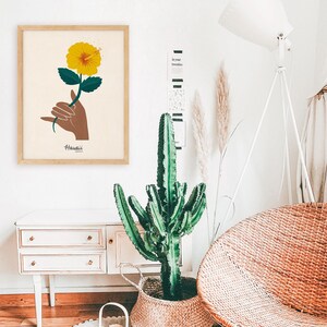 May include: A framed print with a yellow hibiscus flower and a hand making the Hawaiian sign language for "Aloha". The print has the word "Hawaii" written below the image.