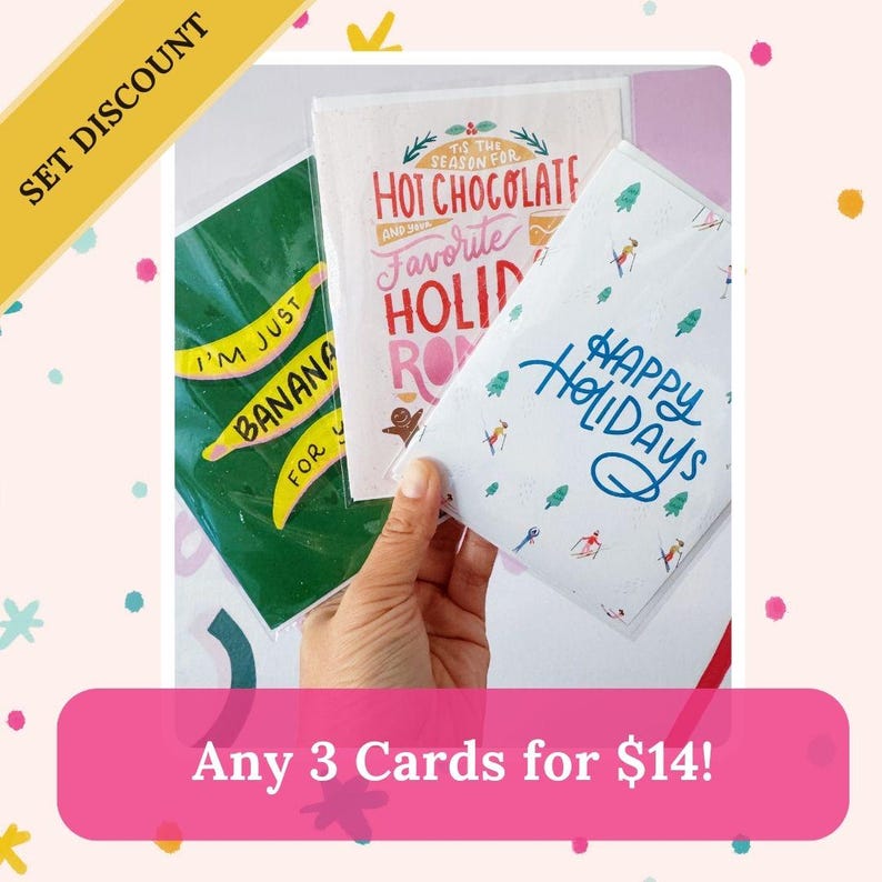 May include: Set of three holiday greeting cards. The cards feature colorful illustrations and text. The text on the cards reads "I'm just banana for you", "Tis the season for hot chocolate and your favorite holiday rom", and "Happy Holidays".