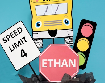 Könnte beinhalten: Ein gelber Schulbus mit einem fröhlichen Gesicht und den Worten "Happy Birthday" auf der Vorderseite. Es gibt auch Verkehrszeichen mit den Worten "Speed Limit 4" und "Ethan" darauf. Die Schilder befinden sich in einem schwarzen Eimer mit schwarzem Seidenpapier.