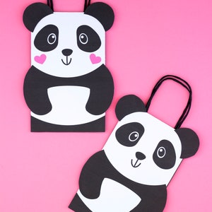 May include: Two panda-themed gift bags with black handles. The bags are white with black panda faces and pink hearts on the cheeks.