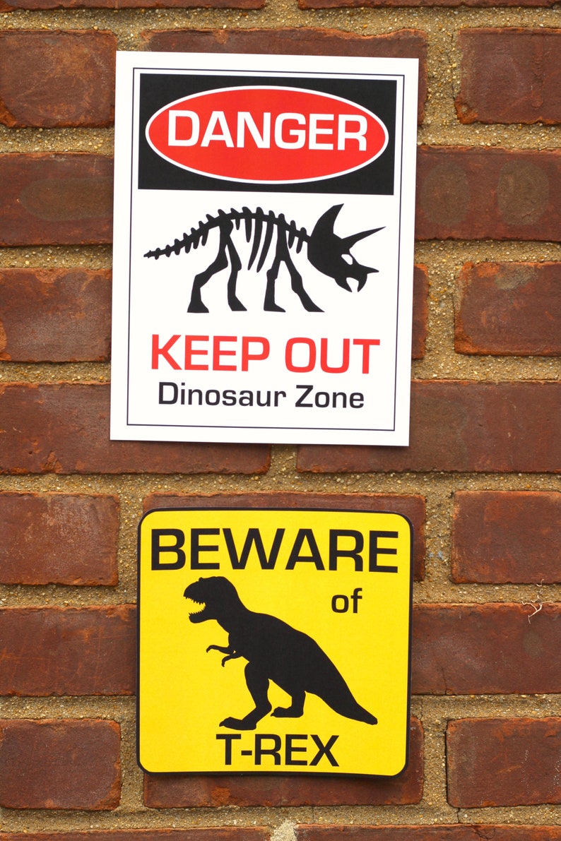 May include: Two warning signs on a brick wall. The top sign is white with black and red lettering. It reads "DANGER KEEP OUT Dinosaur Zone". The bottom sign is yellow with black lettering. It reads "BEWARE of T-REX".