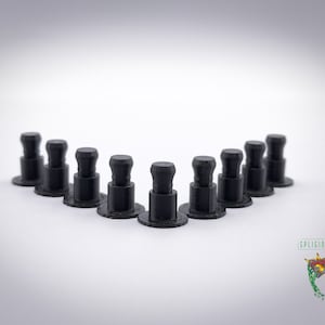 May include: A collection of black plastic furniture pins arranged in a V-shape against a white background. Each pin has a round base, a cylindrical body, and a faceted top. The pins are evenly spaced.