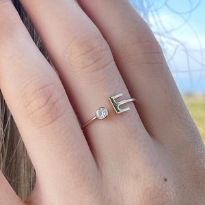 Op de afbeelding: Gouden ring met een enkele heldere steen en de letter "E" op de band.