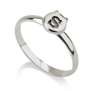 Puede incluir: Un anillo de plata con un dise&ntilde;o de cabeza de gato que presenta la letra "S" en el centro.