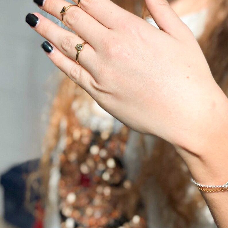 Puede incluir: Un anillo de oro con un peque&ntilde;o dije con la letra "S". El anillo est&aacute; en el dedo de una persona.