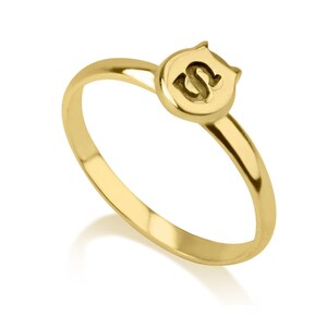 Puede incluir: Un anillo de oro con una letra "S" en relieve en la parte superior. El anillo es simple y elegante.