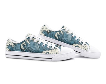 Può includere: Sneakers basse in tela bianca con un motivo a onde blu e bianco. Le scarpe hanno lacci neri e un bordo nero attorno alla suola.
