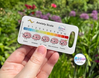 May include: A white anxiety scale card with a handle, featuring a color-coded bar from blue to red, and cartoon brains illustrating levels of anxiety. The scale ranges from 0 to 10, with labels like "Calm" and "Frantic". The card includes the text "Anxiety Scale".