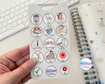 May include: A white communication card with colorful illustrations and text. The card has 16 circles with different images and text, including "Home", "Toilet", "Too Hot", "Coffee", "Food Shop", "Sleep", "Information", "Ear Loope", "Snack & Drink", "Exercise", "Hug", "Pain", "Yes", "No", and "Planit Visuals".