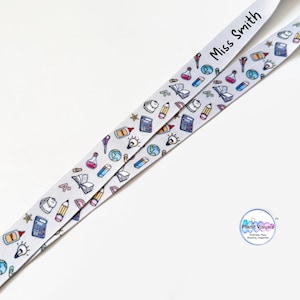 May include: White lanyard with a repeating pattern of school-related icons, including pencils, beakers, and globes. The text "Miss Smith" is printed on the lanyard. The lanyard is designed for teachers or school staff.