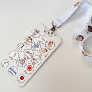 May include: White lanyard with colorful cartoon faces printed on it. A white plastic card with a variety of colorful icons and text is attached to the lanyard. The text on the card includes "Food/Drink", "Toilet", "Information", "Ear Loops", "Sleep", "Pain", "Yes", "No", "Hug", "Help", "Drink", "Eat", and "Coffee".