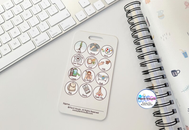 May include: White communication board with 16 round icons featuring various images and text. The icons include images of a tree, a person, a hand, food, a bath tub, a backpack, a phone, and hands in a praying position. The text includes words like "walk", "more", "food", "help", "bath", "bag", "phone", and "thank you". The board also includes the text "Planit Visuals" and "www.planitvisuals.com".