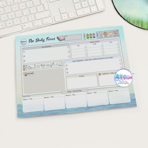 May include: A daily focus planner with a light blue and white design. The planner includes sections for tasks, goals, and time blocking. The text "The Daily Focus" is at the top. A keyboard, pens, and a mousepad are in the background.