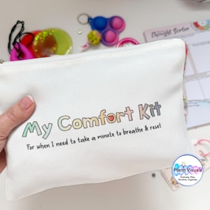 May include: A white canvas pouch with the text "My Comfort Kit" in colourful letters. The pouch includes the phrase "For when I need to take a minute to breathe & reset." Other items are visible, including a pop-it toy and a thought sorter.