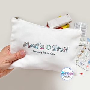 May include: A white canvas pouch with the text "Med's Stuff" in colourful letters. The pouch also has the text "Everything but the doctor!" printed below. Other items in the image include pill packets and a medicine box.