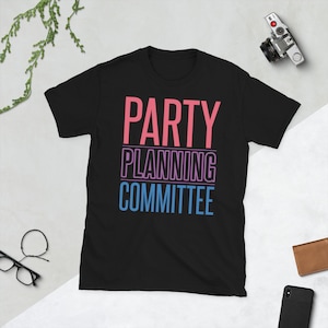 Op de afbeelding: Zwart T-shirt met de tekst "PARTY PLANNING COMMITTEE" in roze, paars en blauw.