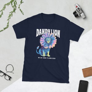 Puede incluir: Camiseta azul marino con un gráfico de un león que lleva una flor de diente de león. El texto "DANDYLION" está por encima del león y "WILD AND FLAWLESS" está por debajo del león.