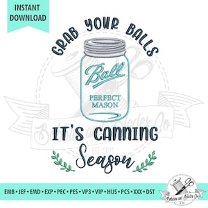 Pode incluir: Um desenho de bordado azul e branco que apresenta um frasco de vidro com o texto "Grab Your Balls It's Canning Season" e as palavras "Ball Perfect Mason" no frasco. O desenho também inclui uma coroa de folhas verdes.