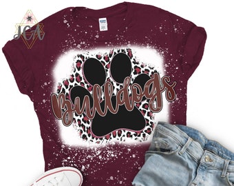 Op de afbeelding: Bordeauxrood T-shirt met een wit splatterontwerp met een zwarte pootafdruk met een roze en witte luipaardprint. Het woord "bulldogs" staat in bruine tekst boven de pootafdruk.