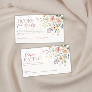 May include: Two white baby shower cards with floral designs and text. One card reads "Books for Baby" and the other reads "Diaper Raffle". Both cards have watercolor flowers in pink, yellow, and purple.