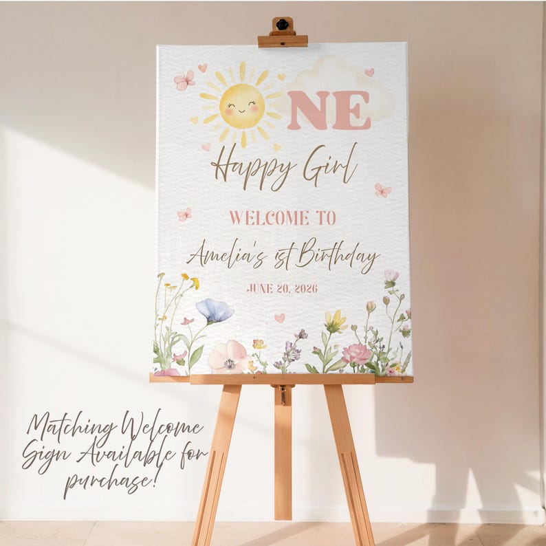 May include: A welcome sign for a first birthday, featuring a smiling sun, butterflies, and floral accents. The sign reads "ONE Happy Girl" and welcomes guests to Amelia's 1st Birthday on June 20, 2026. The sign is displayed on a wooden easel.
