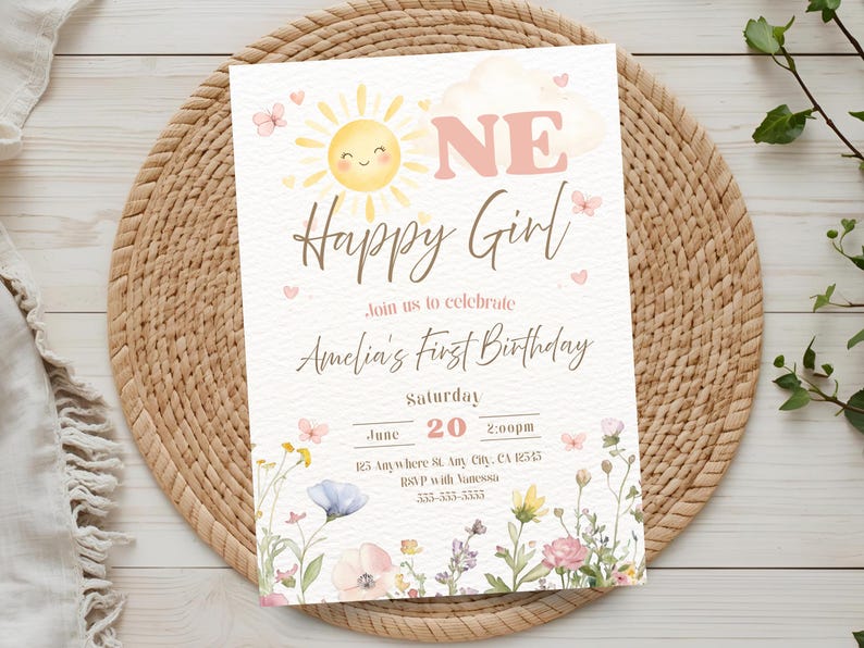 May include: A pastel-colored birthday invitation with a smiling sun, butterflies, and floral accents. The text reads "ONE Happy Girl" and invites guests to Amelia's first birthday on June 20th at 2:00 PM. The invitation is set on a woven placemat.