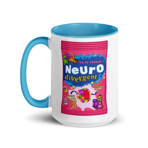Puede incluir: Taza de cerámica blanca con borde y asa azules. La taza presenta un gráfico rosa y azul de una bolsa de caramelos con el texto "You're probably Neurodivergent" y "Sensory Bliss".