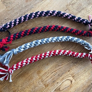 May include: Four braided rope dog toys in different color combinations. The toys are pink and black, red and black, gray and white, and red and white.