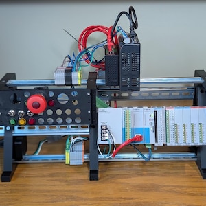 May include: A black metal frame with a red emergency stop button, a variety of electrical components, and a white control panel with the text "Programmable Terminal" on it.