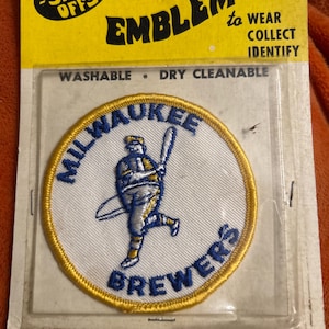 May include: Embroidered Milwaukee Brewers patch with a baseball player graphic. The patch is white with blue and gold accents. The packaging reads "The Show-Offs" and "Emblems to Wear, Collect, Identify."