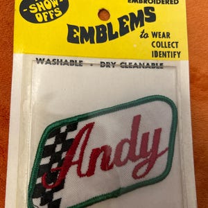 May include: Embroidered "Andy" name patch with a green border and a checkered flag design. The patch is on a yellow and white backing that reads "The Show-Offs" and "Emblems to Wear, Collect, Identify."
