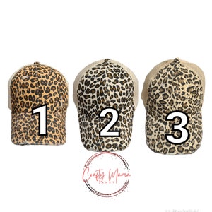 May include: Three leopard print baseball caps with tan mesh backs are displayed. Each cap is numbered with a large white number: 1, 2, and 3. The caps have a brown and tan spotted pattern. The logo "Crafty Mama Planet" is at the bottom.