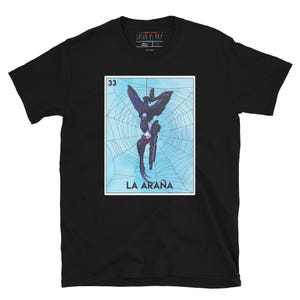 May include: Black t-shirt with a graphic of a blue and purple creature hanging from a spider web. The graphic is surrounded by a blue border and the text "33 LA ARAÑA" is printed below the image.
