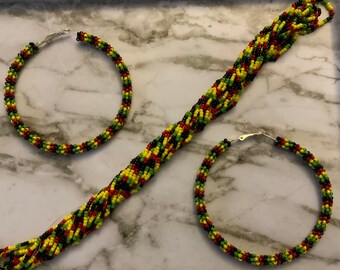 May include: A beaded jewelry set featuring a necklace and two hoop earrings. The beads are in a pattern of yellow, red, black, and green. The earrings have silver-colored clasps. The jewelry is displayed on a marble-patterned surface.
