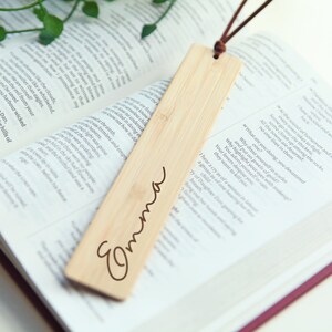 May include: A wooden bookmark with a brown leather string attached. The bookmark is engraved with the name "Emma".
