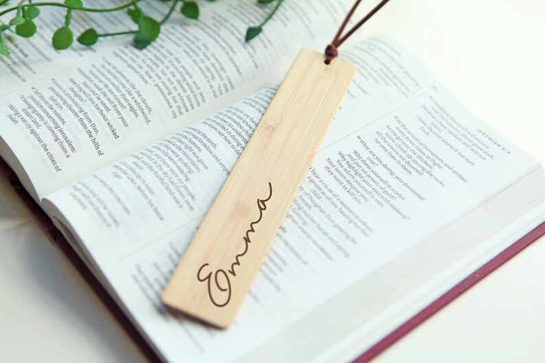May include: A wooden bookmark with a brown leather string attached. The bookmark is engraved with the name "Emma".