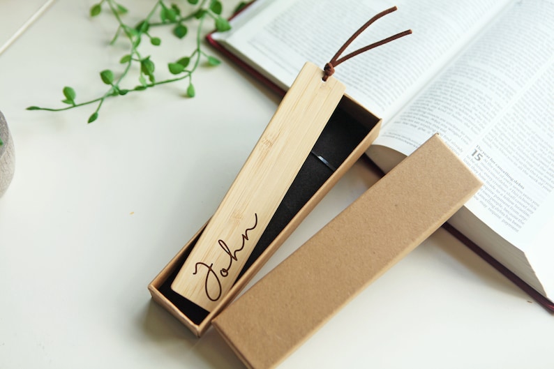 May include: A personalized wooden bookmark with the name "John" engraved on it. The bookmark is in a brown cardboard box with a black velvet lining.