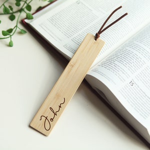 May include: A wooden bookmark with a brown leather string. The bookmark is engraved with the name "John".