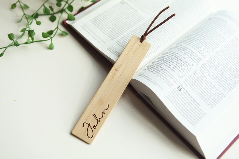May include: A wooden bookmark with a brown leather string. The bookmark is engraved with the name "John".