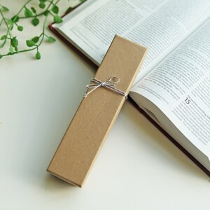 May include: A brown cardboard box with a string bow tied around it. The box is sitting on a white surface next to a closed book.