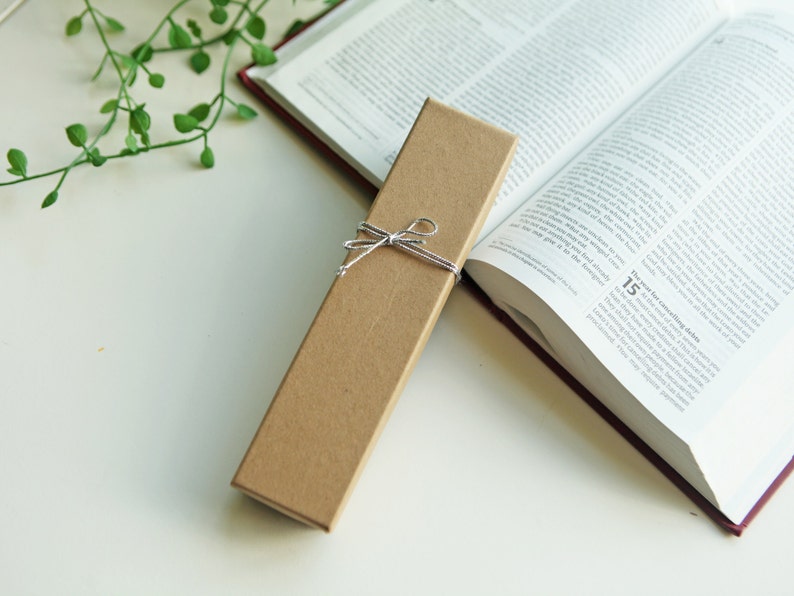 May include: A brown cardboard box with a string bow tied around it. The box is sitting on a white surface next to a closed book.