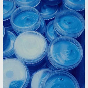 May include: A close-up of several small, clear plastic containers filled with a bright blue substance. The containers are stacked and arranged in a random pattern.