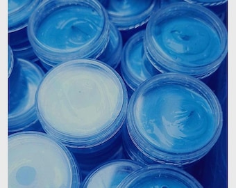 May include: A close-up of multiple small, clear plastic containers filled with a bright blue substance. The containers are stacked and arranged in a random pattern.