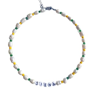 May include: A white pearl necklace with green and yellow beads and the name "SIENA" spelled out in black letters.