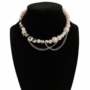 May include: A white pearl necklace with a silver chain and black and white beads with the letters "LOVE" and a yin yang symbol.