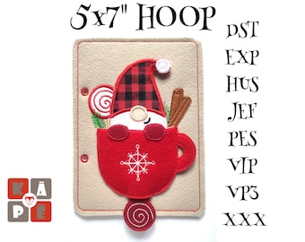 May include: A 5x7 inch hoop with a felt applique of a gnome in a red mug with a candy cane, cinnamon sticks, and a snowflake design. The hoop is beige with a brown border. The text "5x7" HOOP is at the top of the hoop. The text "PST EXP HUS JEF PES VIP VP3 XXX" is on the right side of the hoop.